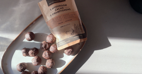 Image features a plate of 5 Mushroom Cacao Bliss Balls next to a bag of Harmonic Arts 5 Mushroom Cacao Herbal Latte.