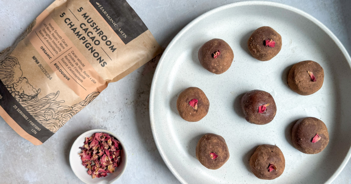 Image features a bag of Harmonic Arts 5 Mushroom Cacao next to a plate of Rose Cacao Truffles. There is a small bowl of rose petals between the bag and the plate.